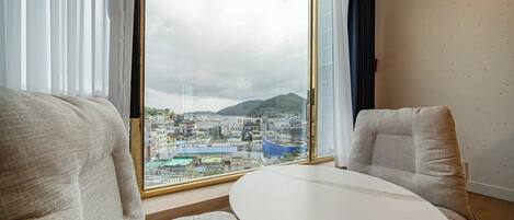 A hotel room with a large window offering a city view, two upholstered chairs, and a small round table.
