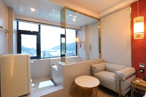 Una habitación de hotel moderna con un ventanal grande, un sofá, una mesita redonda y un espejo.