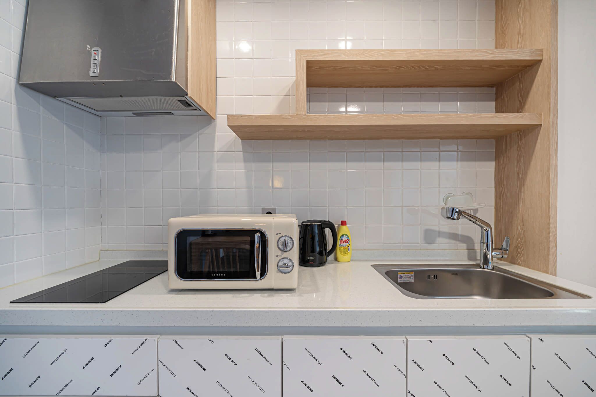 Een keuken met witte tegels, een magnetron, een broodrooster, een spoelbak en houten planken.