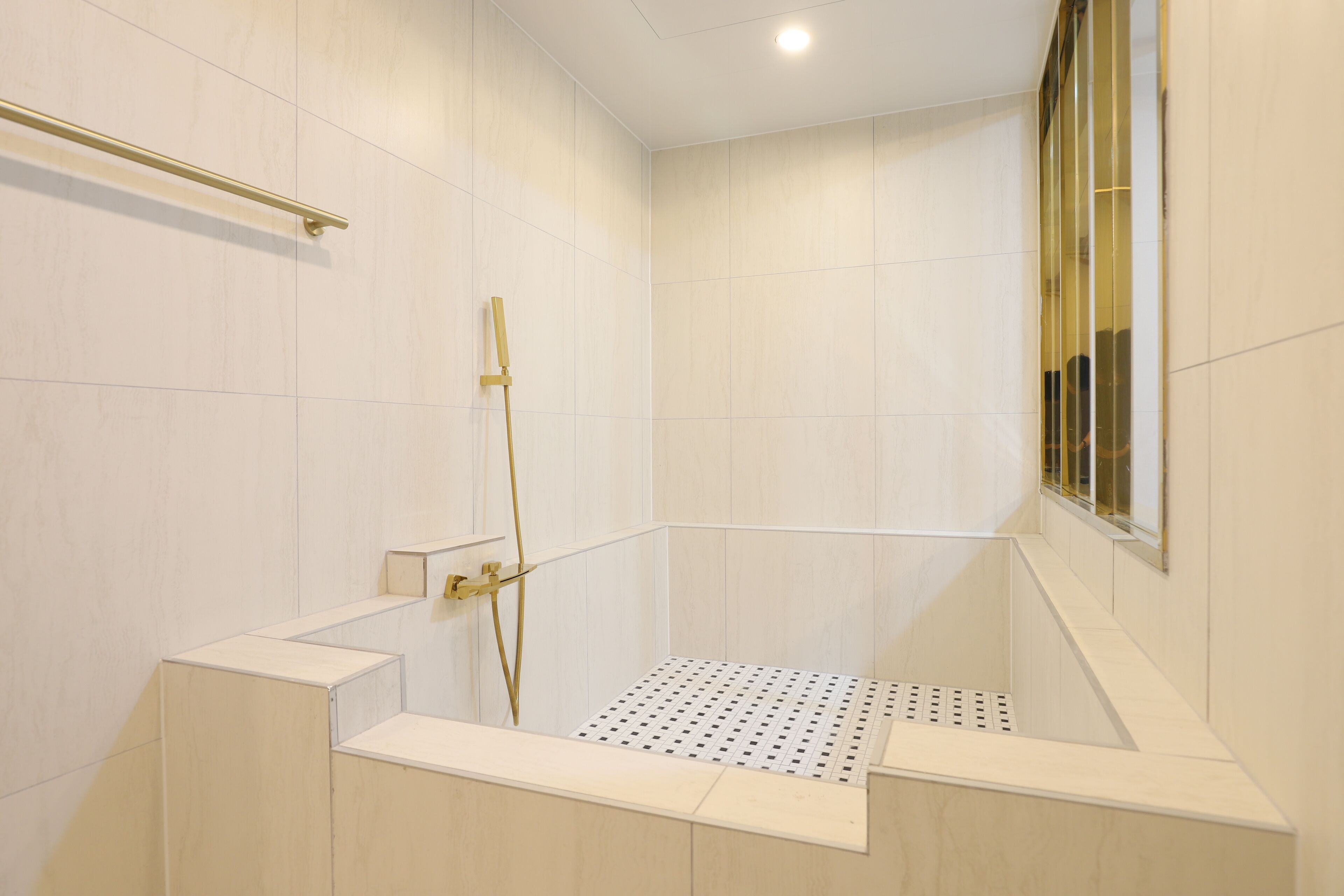 A modern shower area with a glass door, a gold showerhead, and a tiled floor.