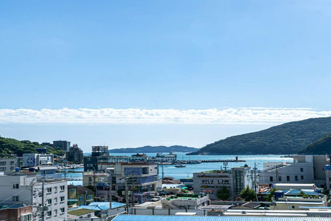 A coastal cityscape with buildings, a harbor, and a mountainous backdrop.