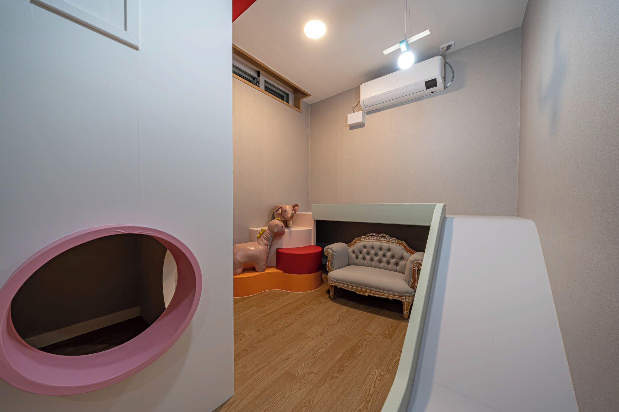 A room with a pink circular play area, a tufted armchair, and a white cabinet.