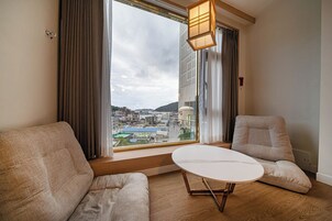 Una sala de estar moderna con un ventanal grande, dos sofás color beige, una mesa blanca y una lámpara colgante.