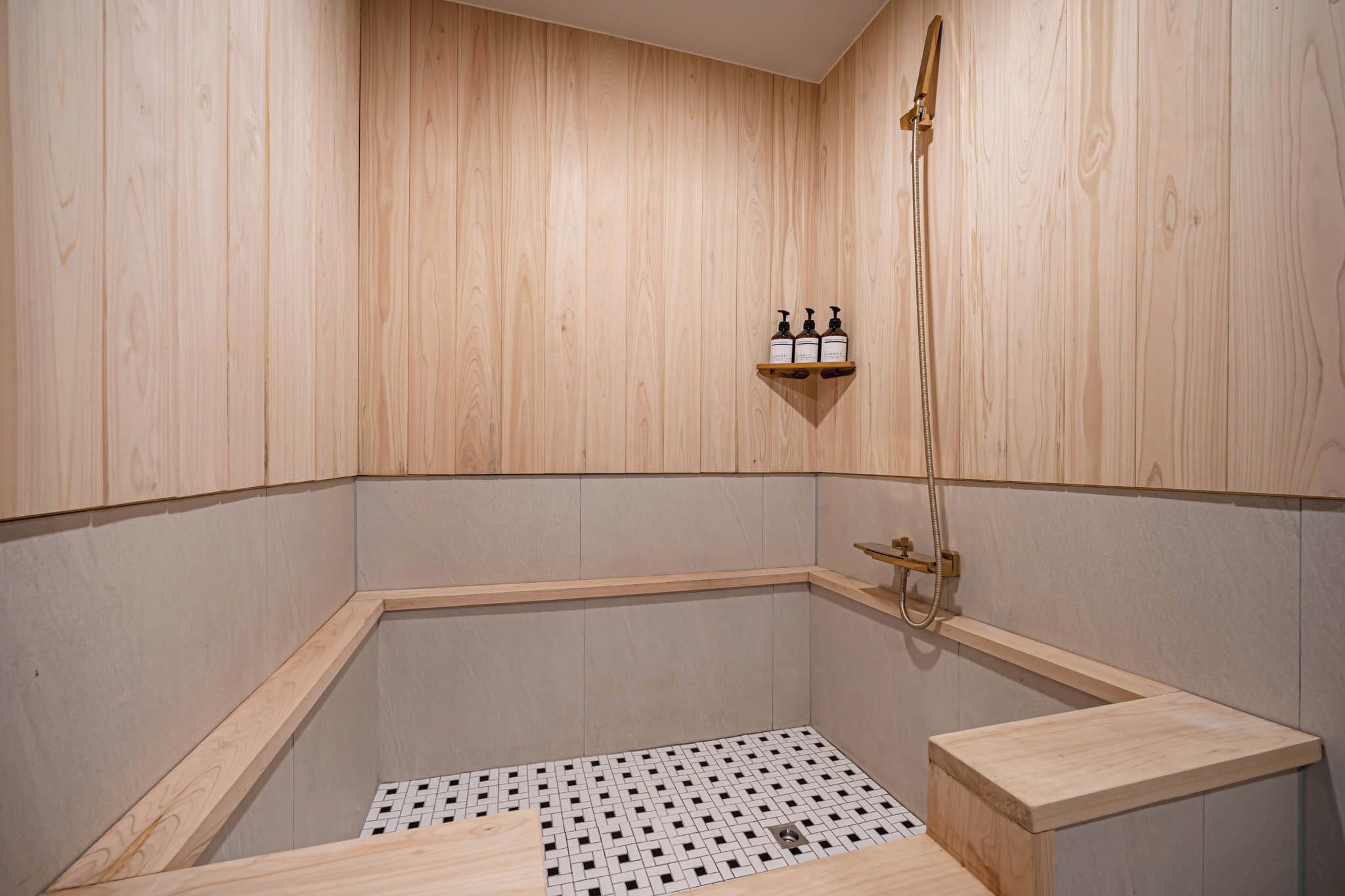 Une salle de bain aux murs lambrissés, avec une douche d’angle, une étagère contenant des articles de toilette et un sol carrelé.