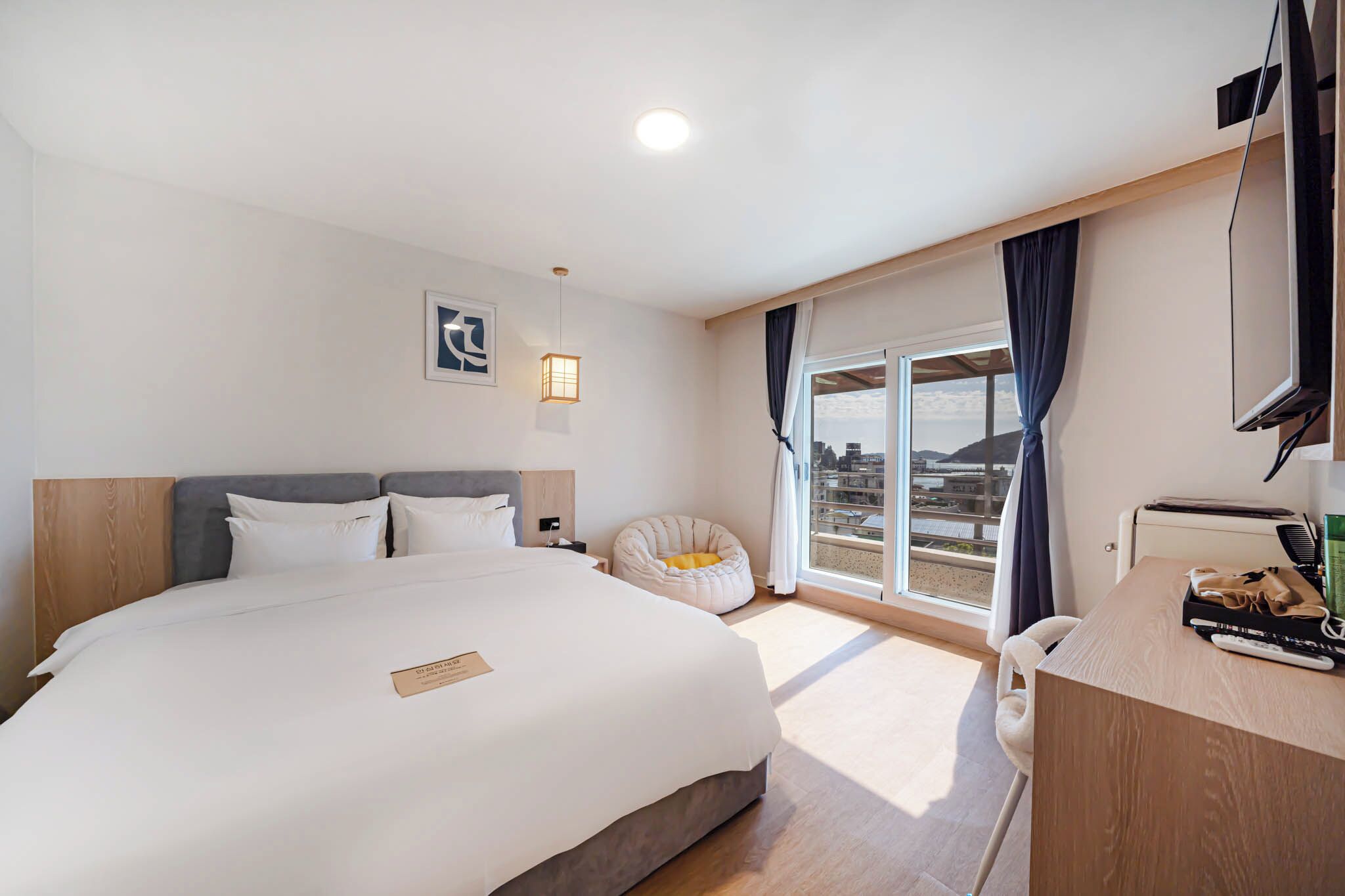 A hotel room with a large bed, a desk with a telephone, and a view of the city through the window.