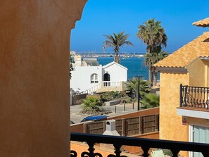 A coastal view with a white building, palm trees, and a marina in the background.
