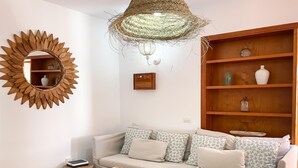 A living room with a sofa, a round mirror, a wooden shelf, and a hanging light fixture.