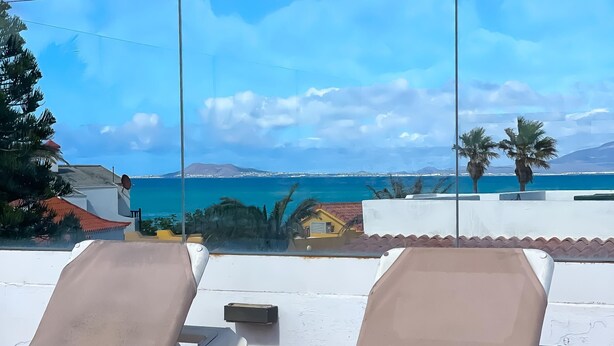 Two lounge chairs on a terrace with a view of the sea and distant mountains.