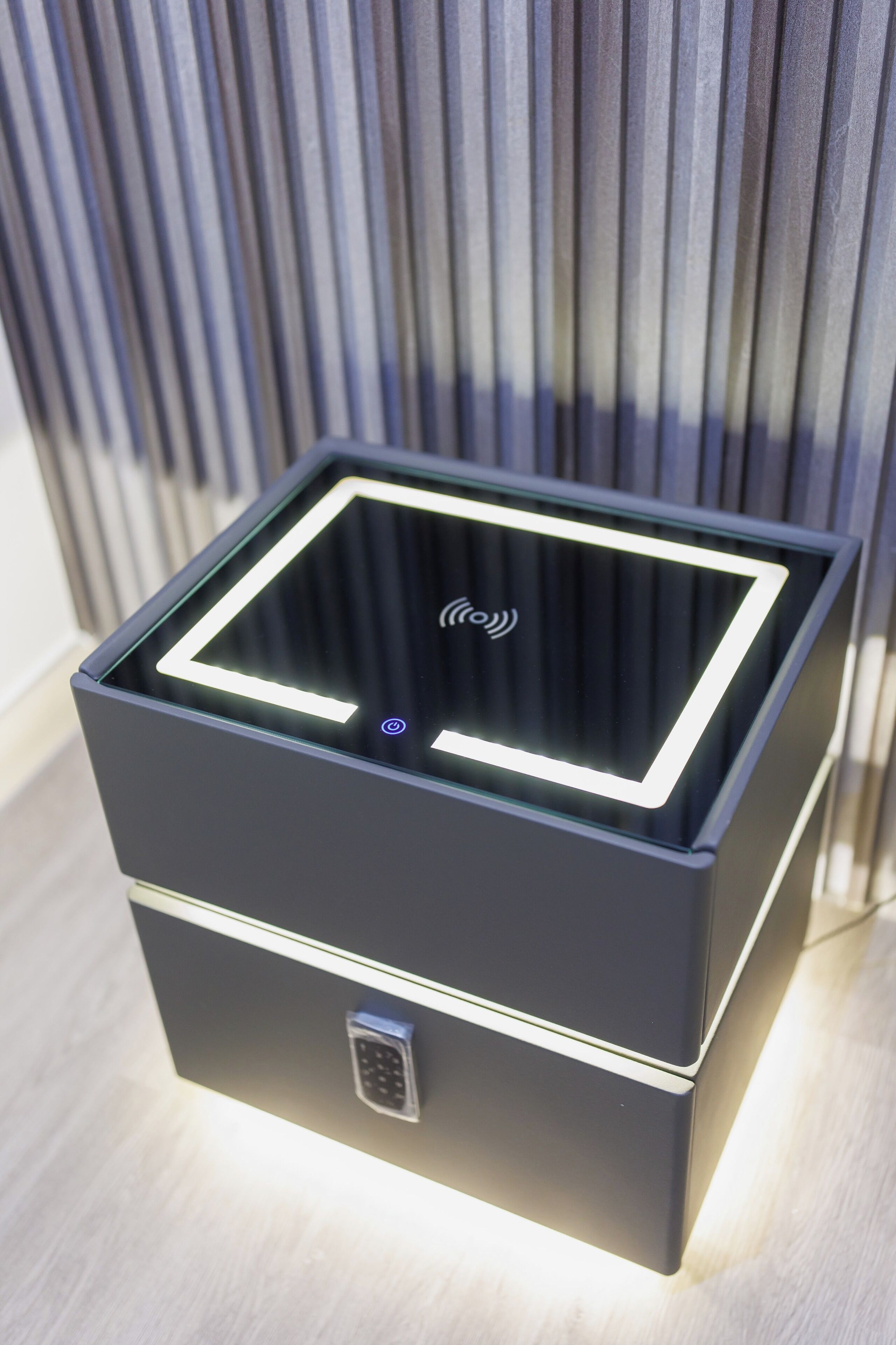 Un appareil électronique moderne, de forme carrée, doté d’un dessus en verre et d’un clavier, posé sur une surface en bois.