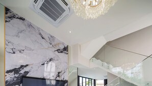 Een moderne woonkamer met een grote flatscreen televisie, een marmeren wand en een glazen wenteltrap naar een balkon.