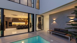 Een modern interieur met een zwembad, een eethoek en een zithoek met een bank en een plant.