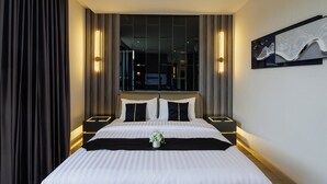 Hotelkamer met een groot bed, twee nachtkastjes, een raam met gordijnen en een aan de muur bevestigd kunstwerk.