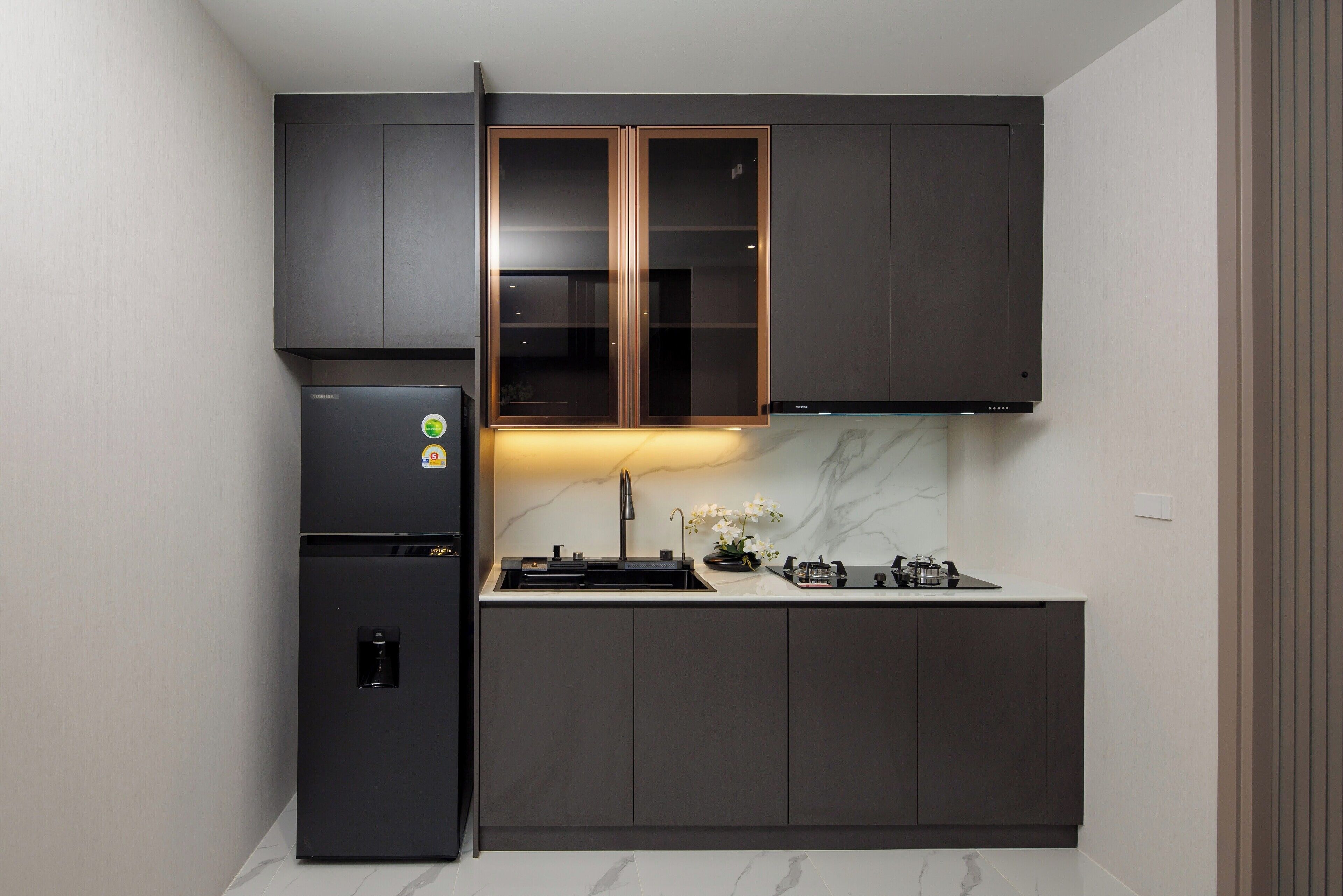 A compact kitchen with dark cabinetry, a built-in refrigerator, a sink, and a gas stove.