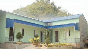 A building with a green and blue exterior, multiple windows, and a small garden area with potted plants and flowers. - Viet Hoang Hostel Moc Chau - BAYLUXURY (Thao Nguyen)