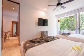 Ein Hotelzimmer mit zwei Betten, einem Fernseher, einem Deckenventilator und einem großen Fenster mit Blick auf Bäume.