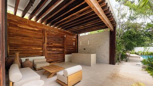 Un patio exterior con mobiliario de madera, pared de ladrillo y piscina.