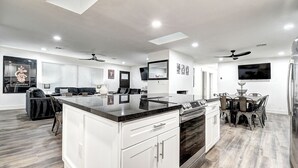 A modern kitchen with white cabinetry, a central island, and a dining area with a table and chairs. - ScottsdaleStays Grand Chateau - 12BR Resort Estate - 500K Pool + Courts (Phoenix)