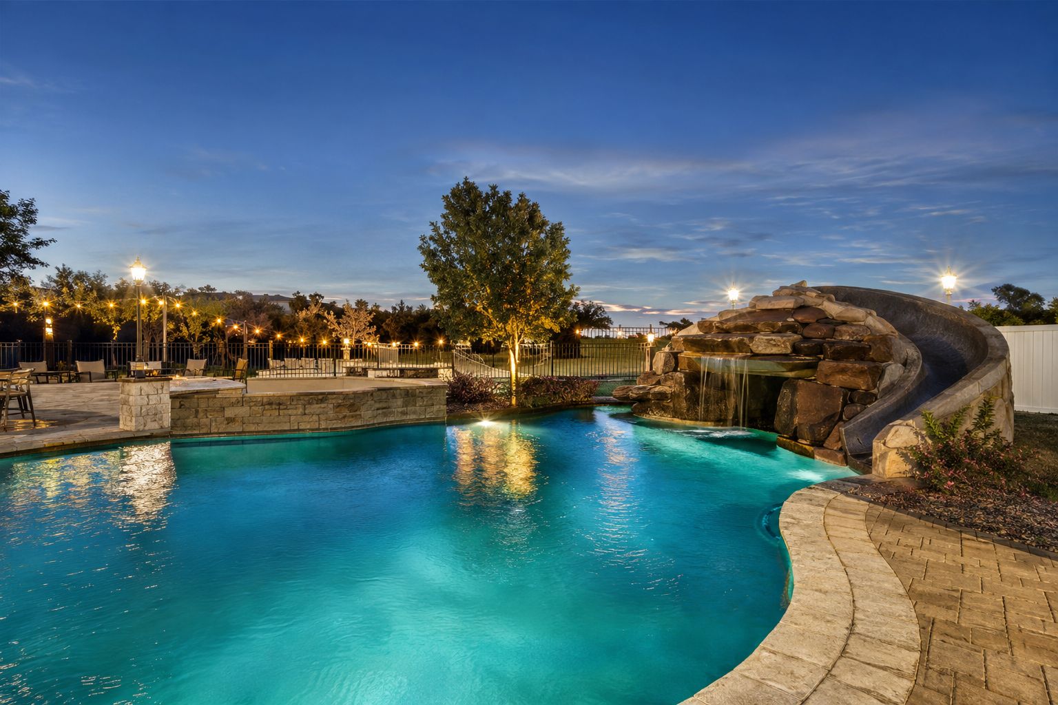 A swimming pool with a waterfall feature, surrounded by a paved deck and outdoor seating.
