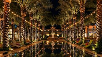 A poolside area with palm trees and lounge chairs, reflecting a building in the background.
