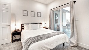 A neatly arranged bedroom with a large bed, a bedside table with a lamp, and a view through a glass door to an outdoor area. - ScottsdaleStays Grand Chateau - 12BR Resort Estate - 500K Pool + Courts (Phoenix)
