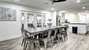 A modern kitchen with white cabinets, a central island, and a dining area with a large table and chairs. - ScottsdaleStays Grand Chateau - 12BR Resort Estate - 500K Pool + Courts (Phoenix)