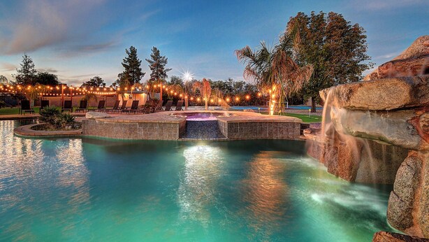 A swimming pool with a waterfall feature, surrounded by lounge chairs and a stone structure. - ScottsdaleStays Grand Chateau - 12BR Resort Estate - 500K Pool + Courts (Phoenix)