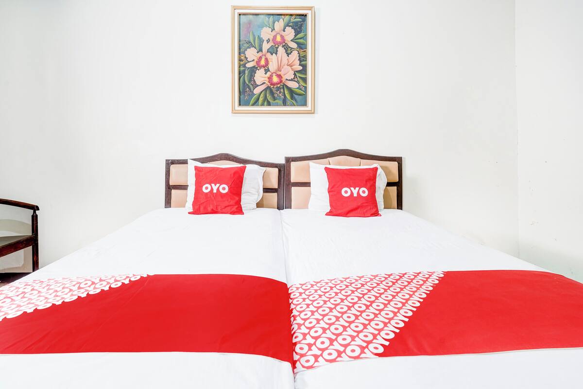 A double bed with two pillows, a red and white bedspread, and a painting on the wall.