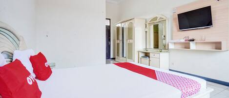 A hotel room with a large bed, a TV mounted on the wall, a vanity with a mirror, and a red and white patterned bed runner.