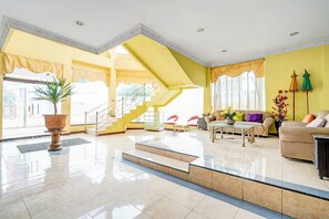 A spacious living area with a staircase, a large potted plant, and a sofa set. - Collection O Kauman Near Stasiun Pekalongan Formerly HOTEL DIAN CANDRA (Wiradesa)