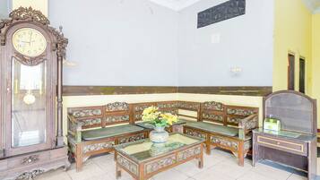 A traditional room with a wooden sofa set, a glass-top coffee table, a large ornate clock, and a mirror.
