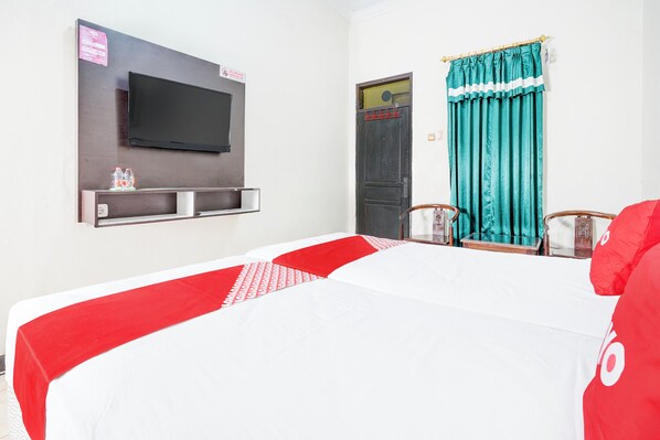 A hotel room with a bed, a television mounted on the wall, a door with a sign, and a window with curtains.