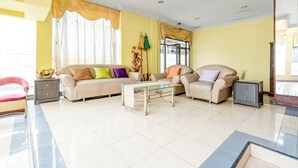 Un amplio salón con un sofá beige, una mesita de centro de vidrio y una mesita auxiliar.