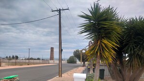 Une route bordée d’un poteau électrique, une structure haute visible au loin, et une clôture couverte de végétation.