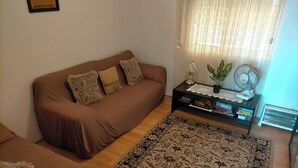 Un salon avec un canapé marron, un tapis à motifs, une petite table d’appoint avec un ventilateur et un radiateur.