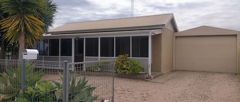 A building with a covered patio area, a fenced garden with large plants, and a garage.