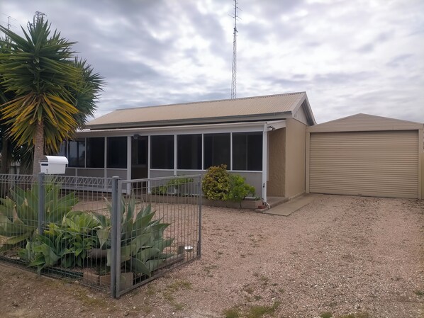 A building with a covered patio area, a fenced garden with large plants, and a garage.