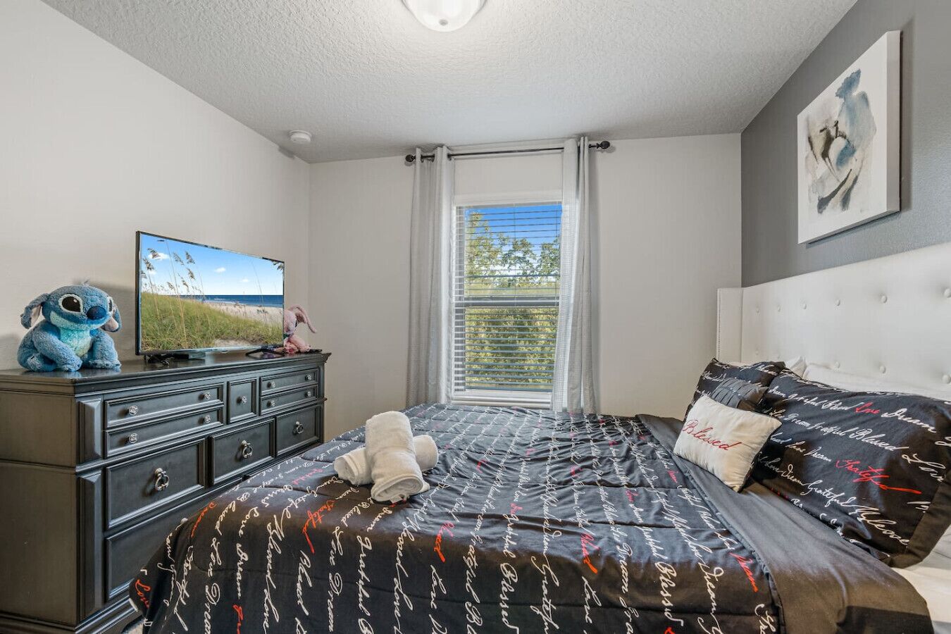 A bedroom with a bed, a dresser, a television, and a window with curtains.