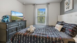 A bedroom with a bed, a dresser, a television, and a window with curtains.