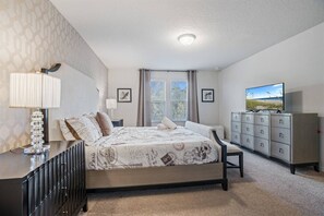 A bedroom with a bed, bedside table, lamp, dresser, television, and framed pictures on the wall. - Luxury 5BDR House w/ pool - 8863 (Kissimmee)