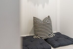 A corner with a white wall, a black and white patterned pillow, and a dark cushioned bench.