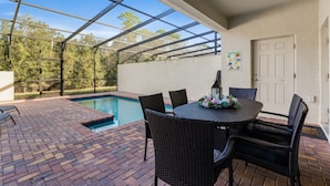 An outdoor patio with a pool, a table with chairs, and a door.