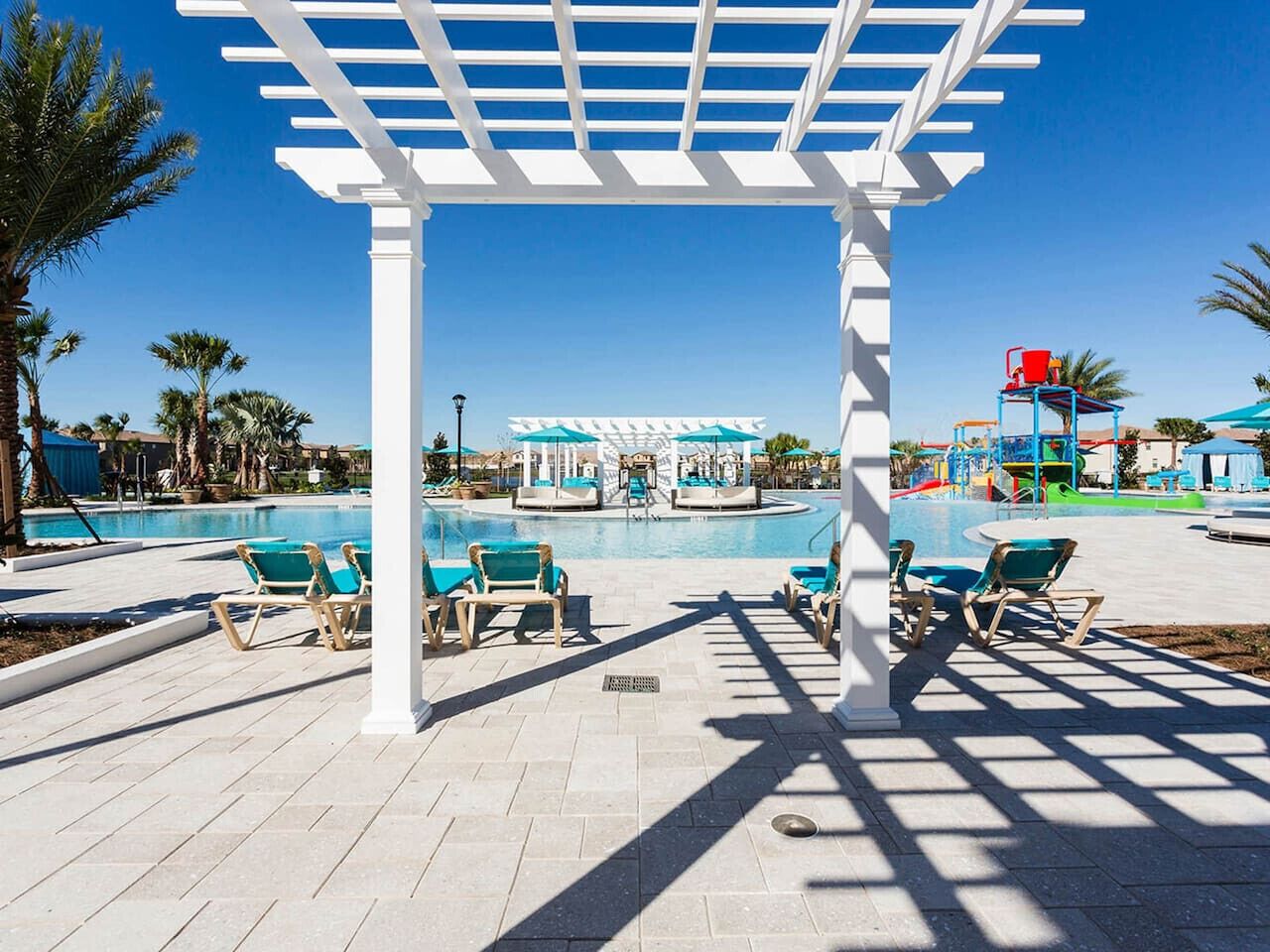 Ein Poolbereich mit Liegestühlen, einer Pergola und einer Spielanlage für Kinder.