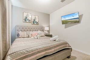 A bedroom with a bed, pillows, a stuffed toy, a TV, and artwork on the wall.