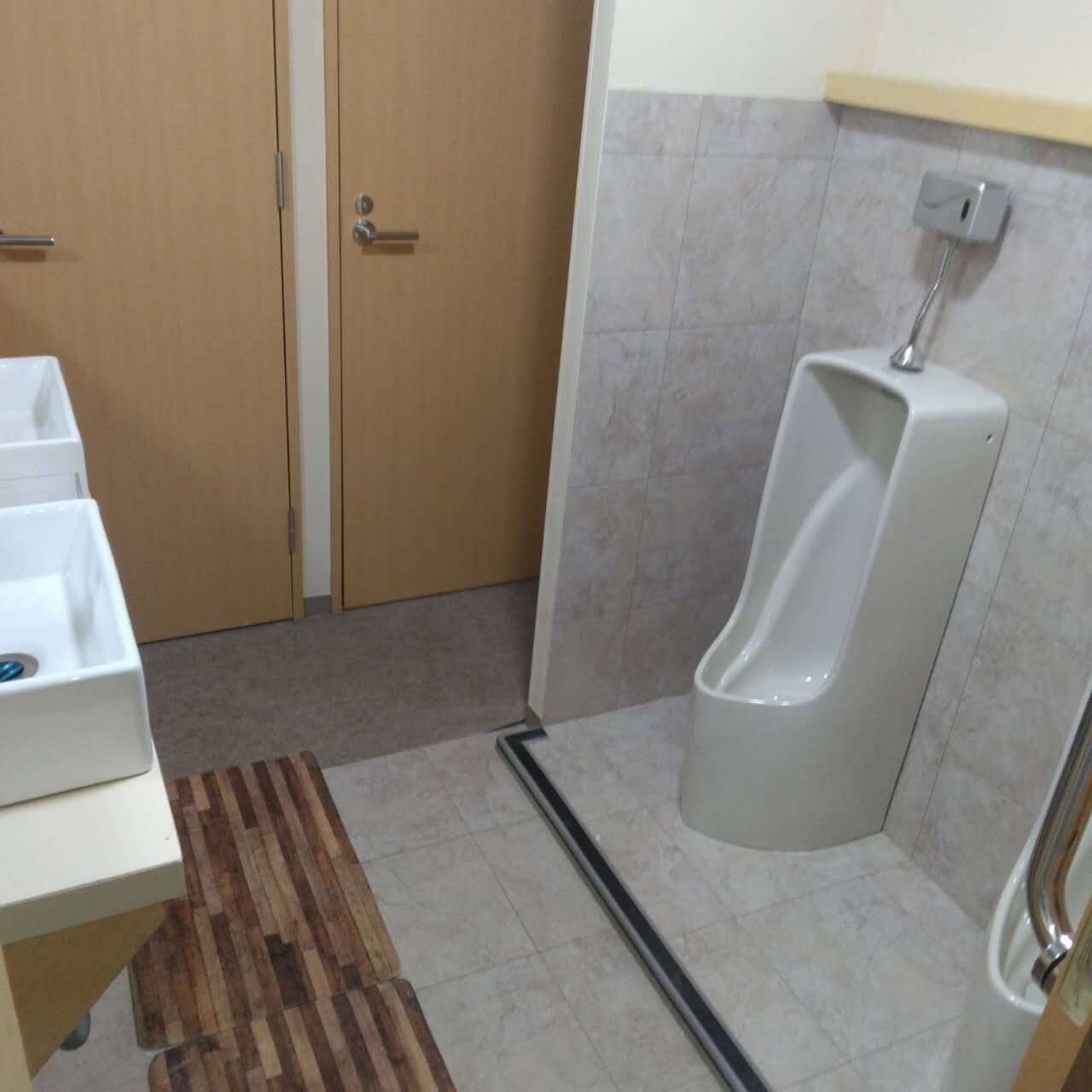 Un baño de hombres con un orinal, un banco de madera y piso de baldosas.