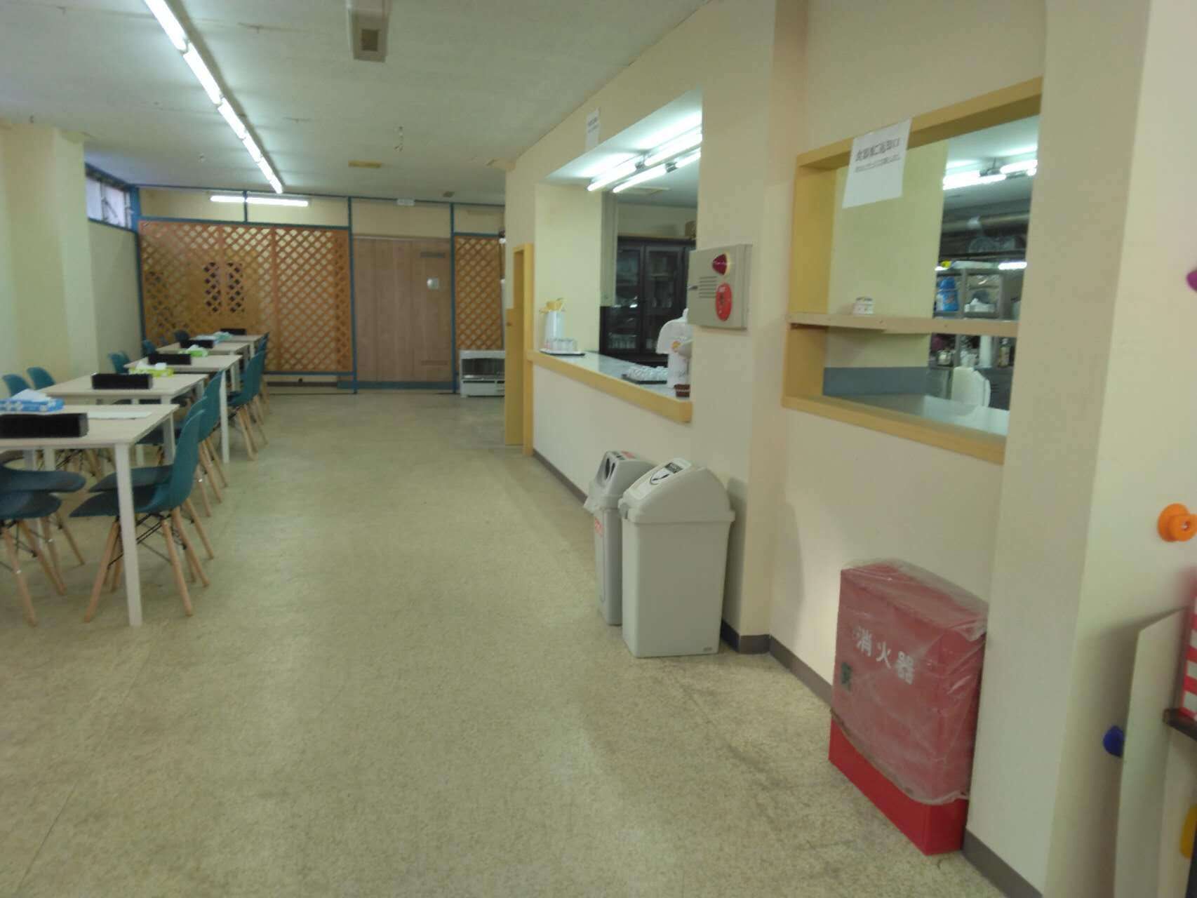 A classroom with rows of desks and chairs, a teacher's desk, a trash bin, and a fire extinguisher.