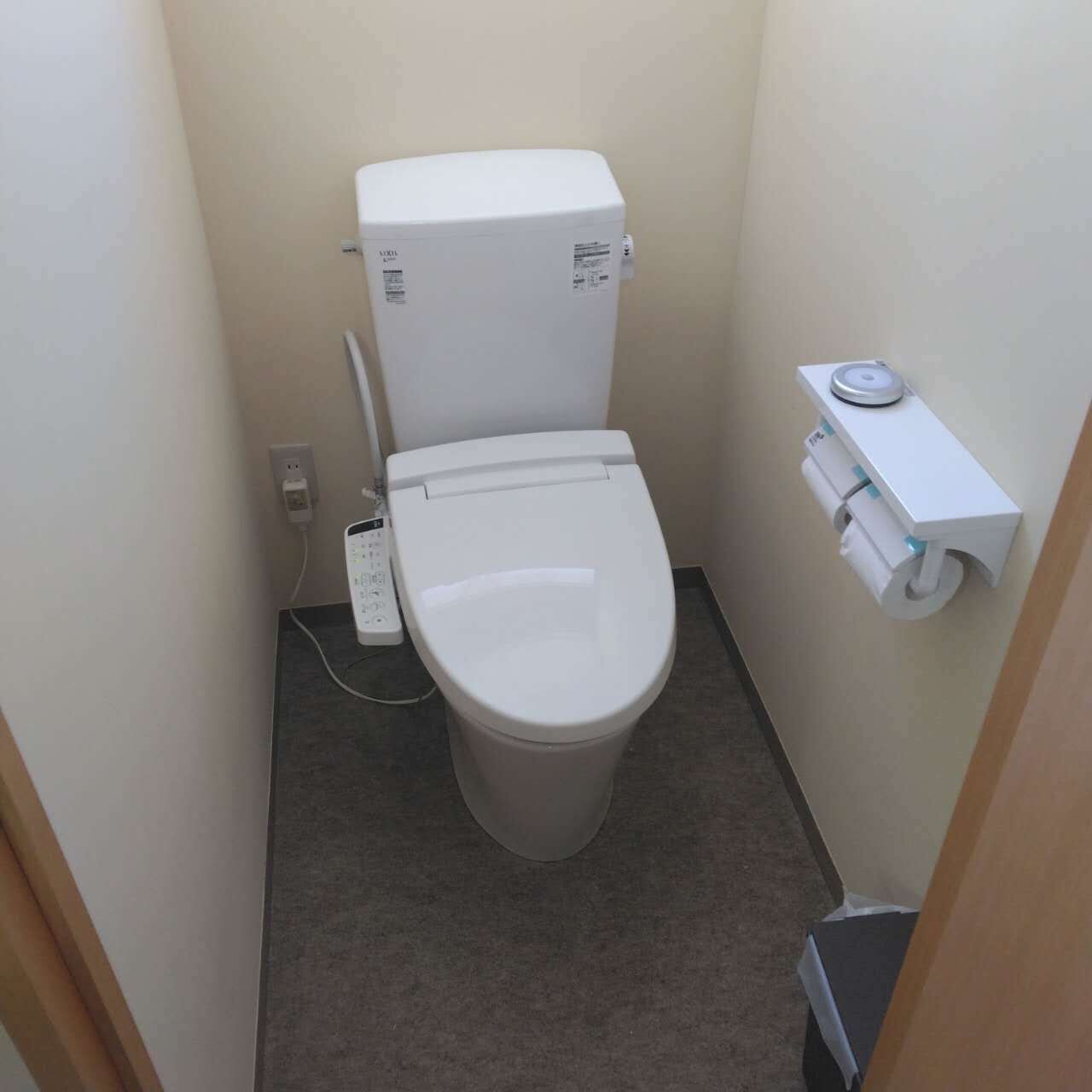 Un baño pequeño y funcional con un inodoro blanco, un dispensador de papel higiénico en la pared y un enchufe.