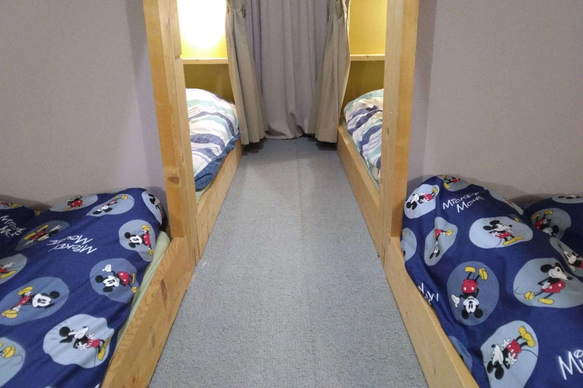 Une petite pièce avec deux lits superposés, chaque lit étant recouvert d’une couette aux motifs de Mickey Mouse.
