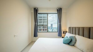Un dormitorio con una cama grande, vistas de la ciudad a través de una ventana y una mesita de noche con una lámpara.