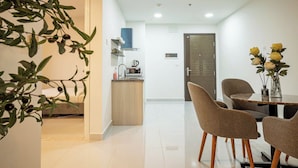Una cocina moderna con horno integrado, cafetera y un mueble pequeño. Hay un comedor con mesa y sillas, y una puerta que conduce a otra habitación.