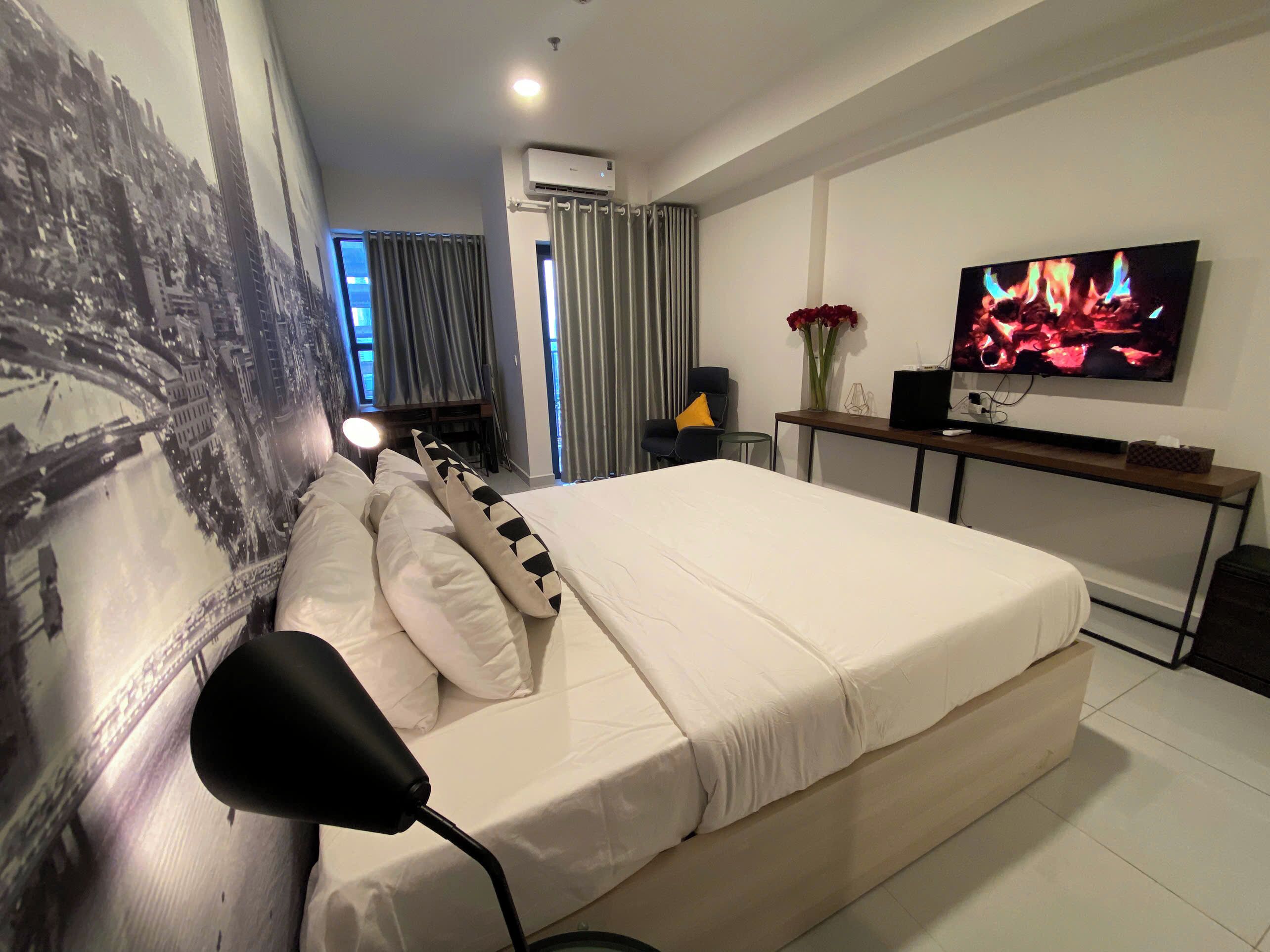 A hotel room with a large bed, a desk with a TV, and a wall mural.